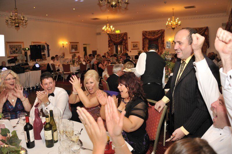A group of people are sitting at a table with their hands in the air.