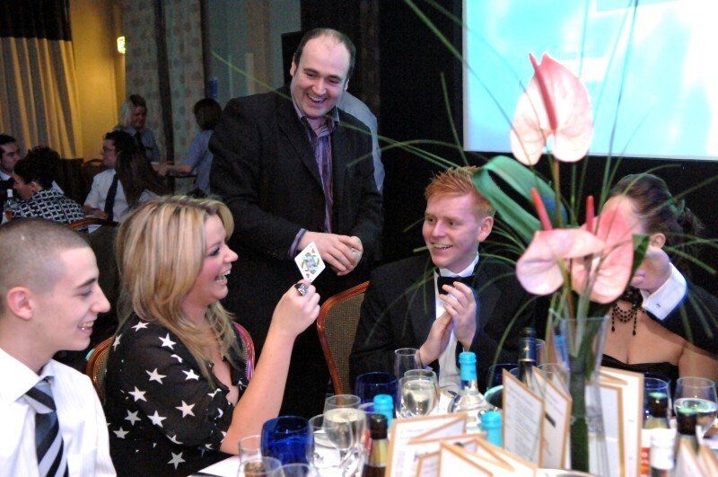 A group of people are sitting at a table watching a man perform a trick