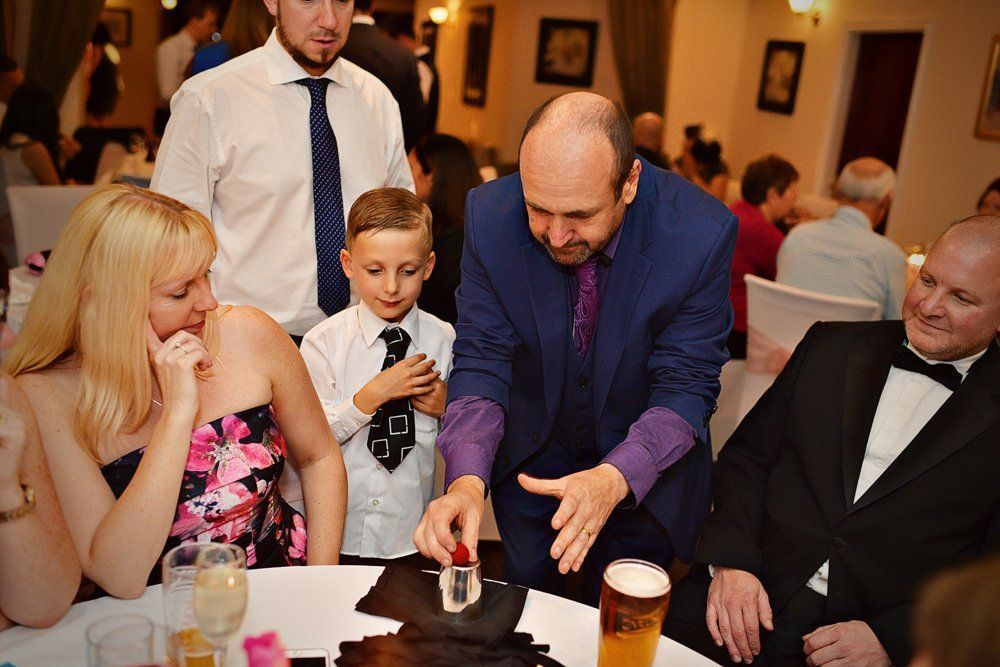 A group of people are sitting at a table watching a man perform a trick.
