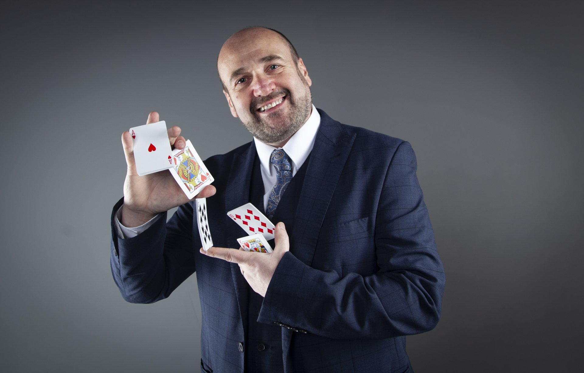 A man in a suit and tie is holding two playing cards in his hands.