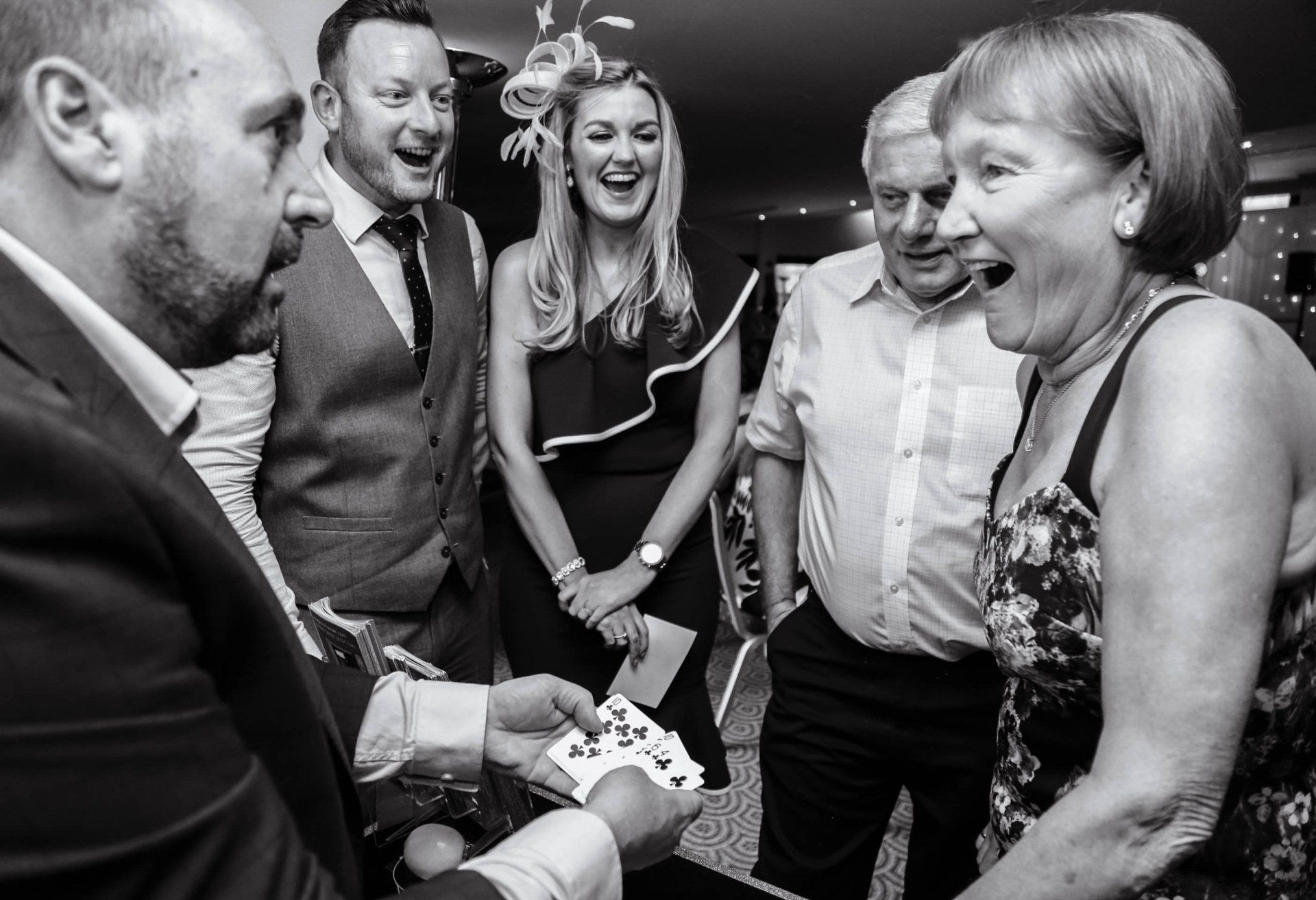 A group of people are standing around a man holding playing cards.