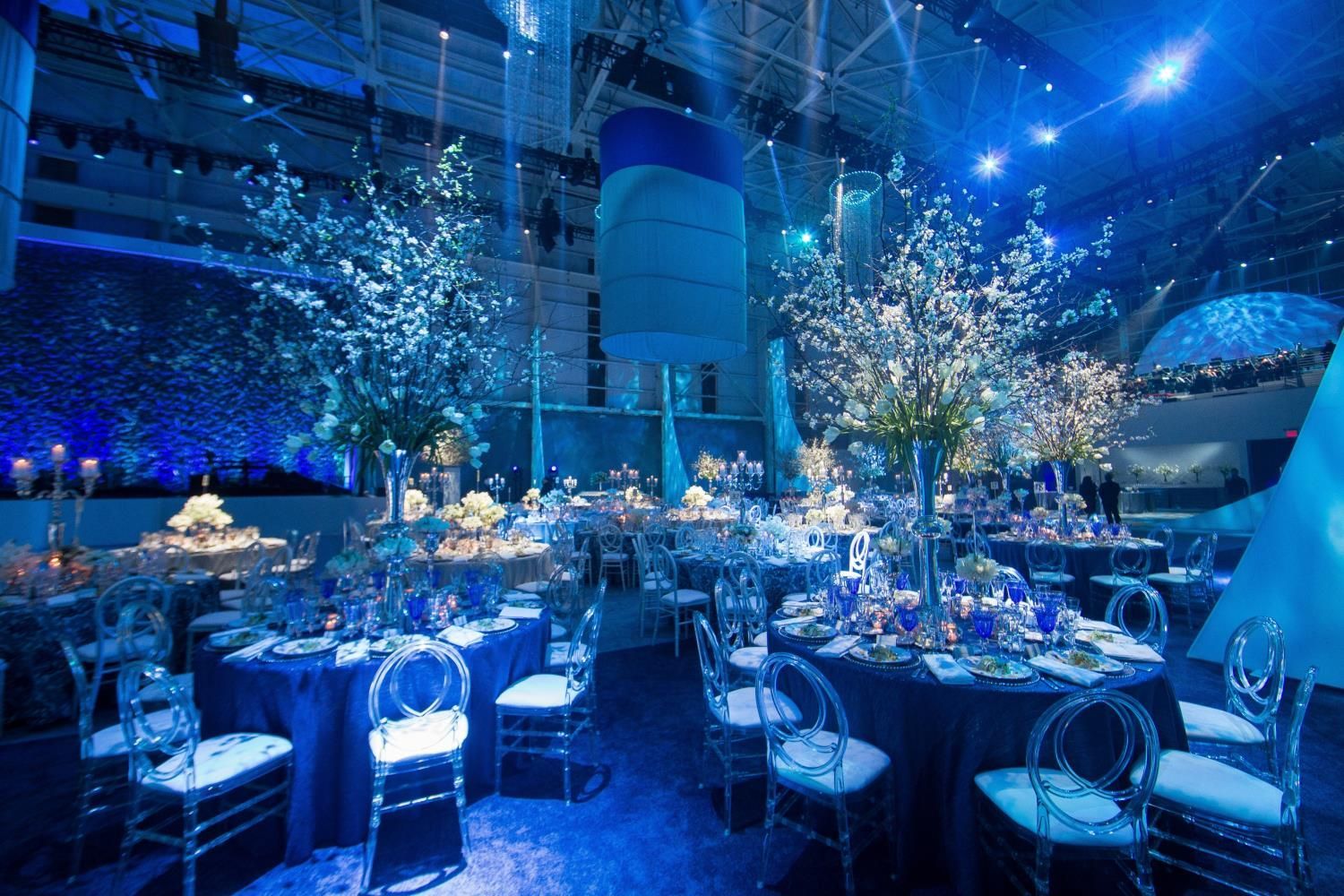 Elegant event space, tables set for a party, blue and white decor, translucent chairs.