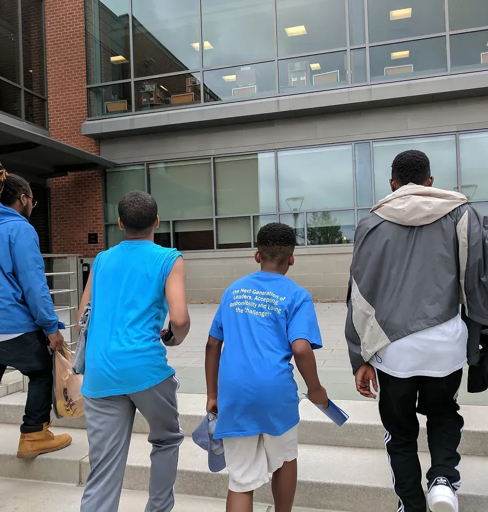 Four people walking up steps towards a building with glass windows, all wearing blue shirts or jackets.