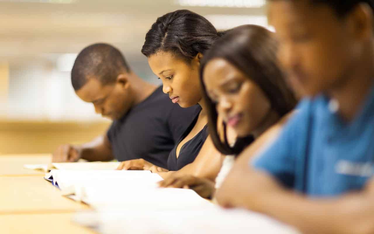 Students reading books at a table, focused and studying, in a library setting.