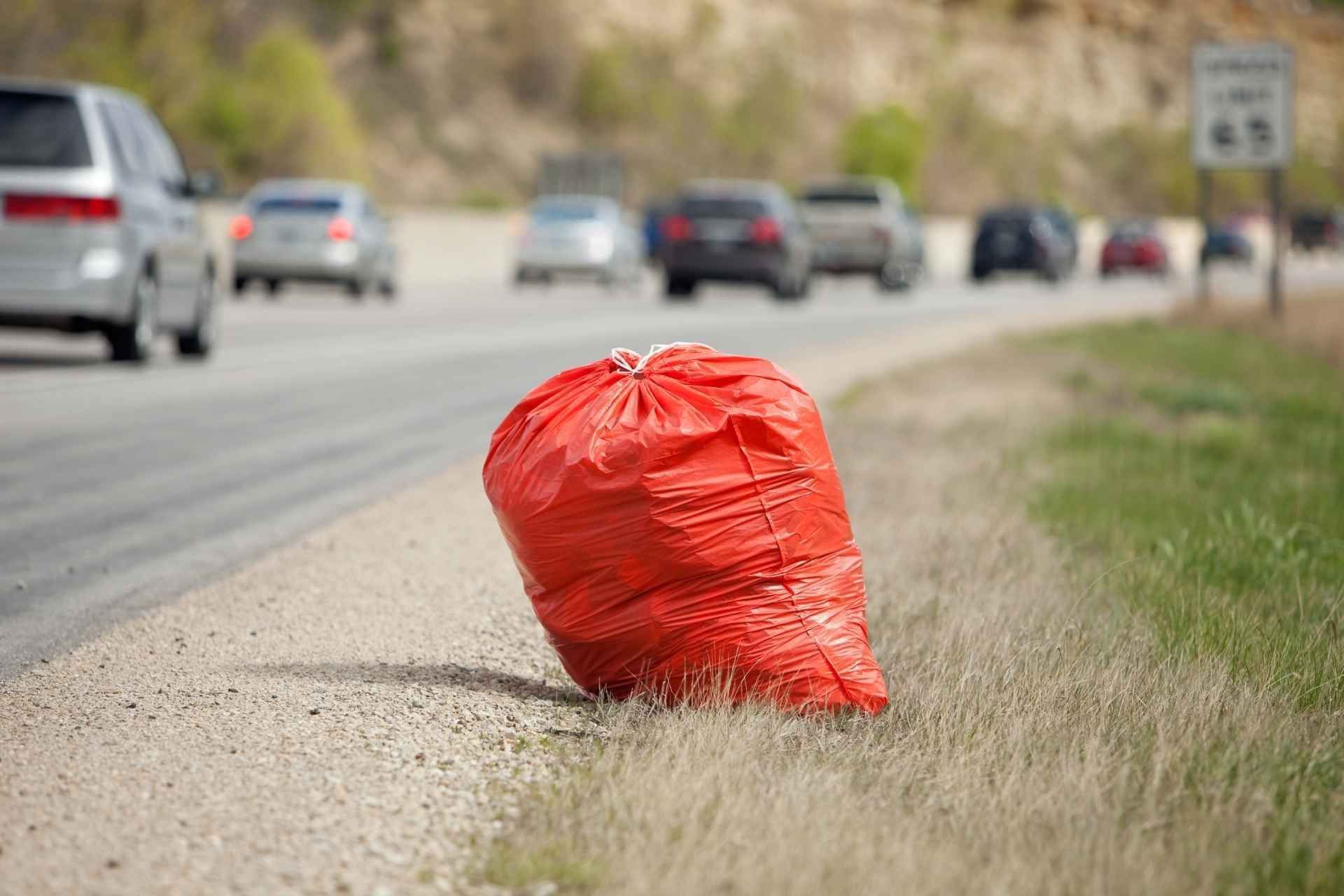 Red trash bag on side of a highway with passing cars and a speed limit sign.