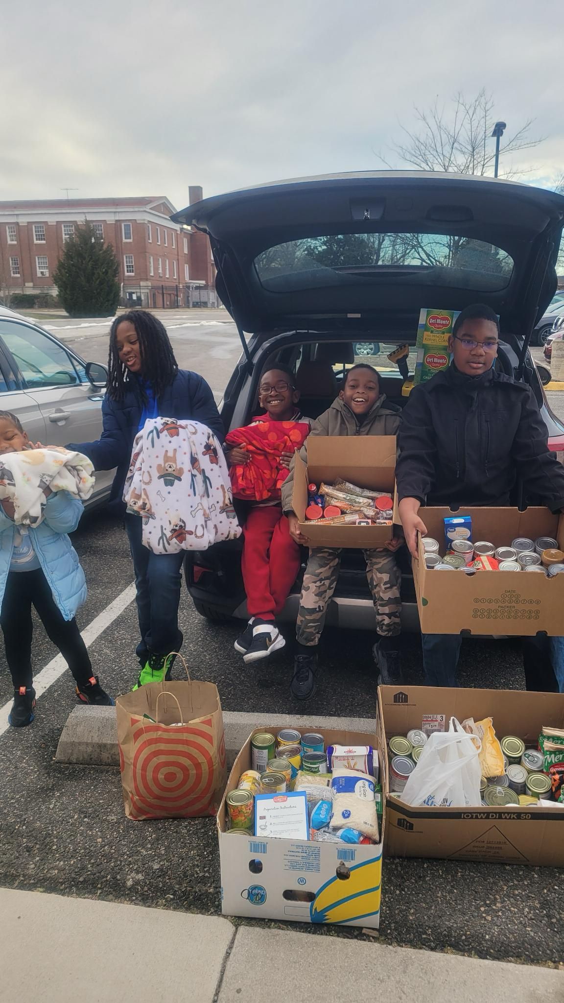 People unloading food donations from a car trunk; boxes and bags full of canned goods and clothes.