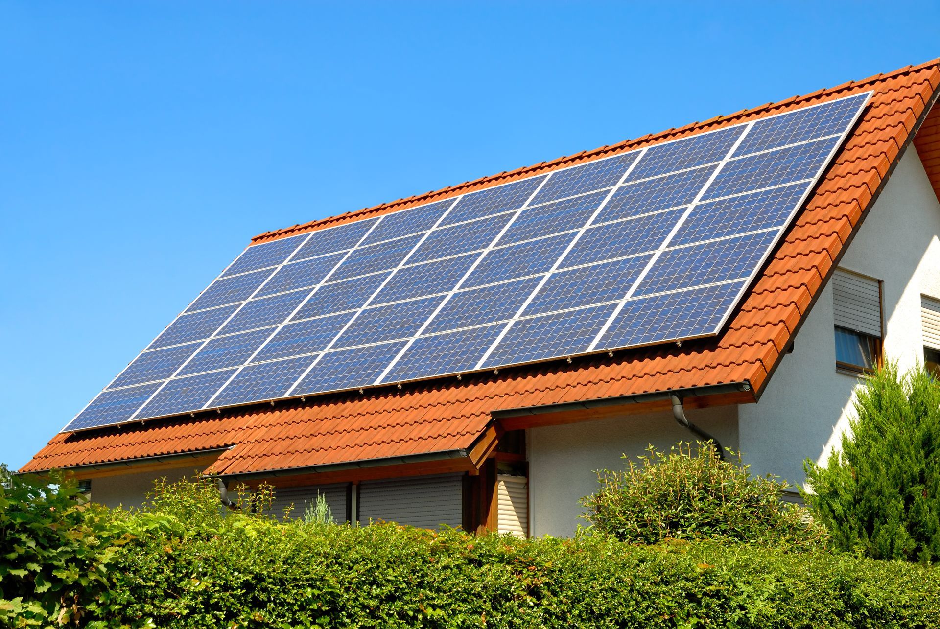 Solarpaneele auf dem roten Ziegeldach eines weißen Hauses vor einem klaren blauen Himmel.