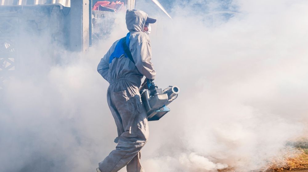 Person in protective gear spraying fog or smoke outdoors with a handheld machine