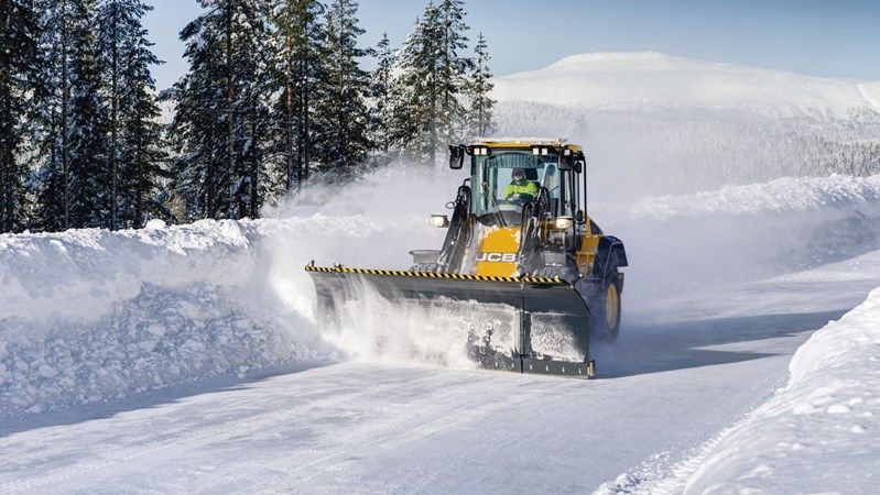 A snow plow is driving down a snow covered road.