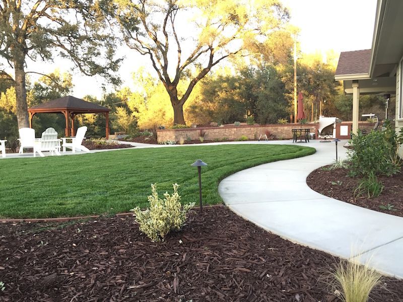 A concrete walkway leading to a gazebo in the backyard of a house.