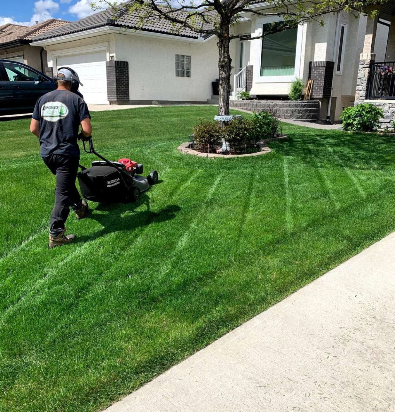 A man is mowing a lush green lawn in front of a house.