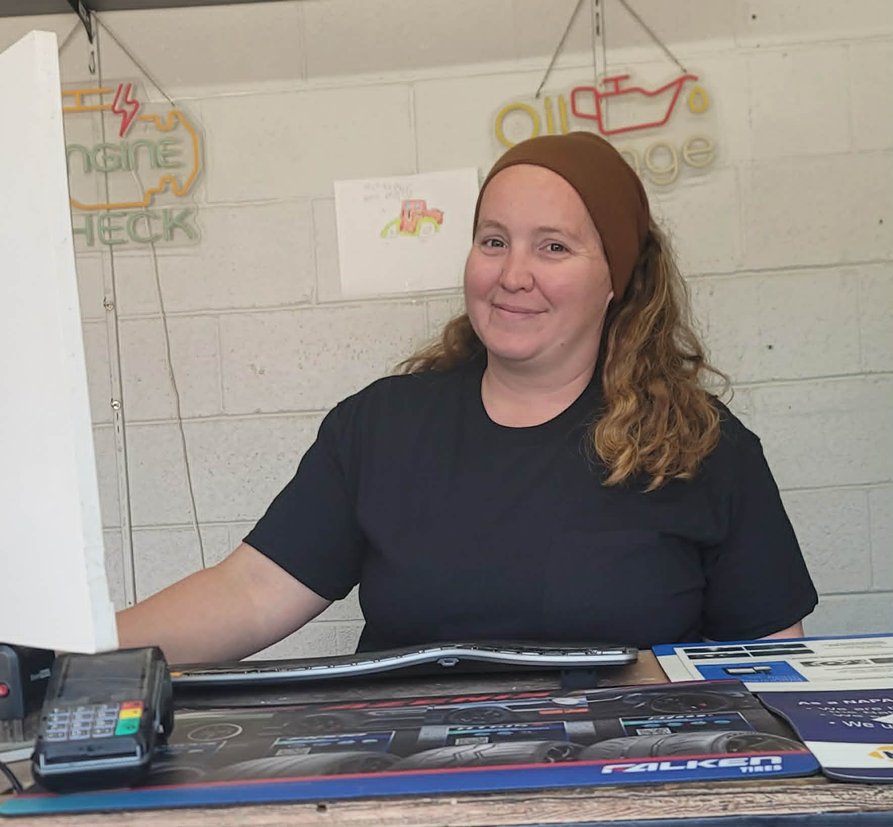 Smiling clerk behind a counter in a black shirt, with a payment terminal and colorful signs in the background