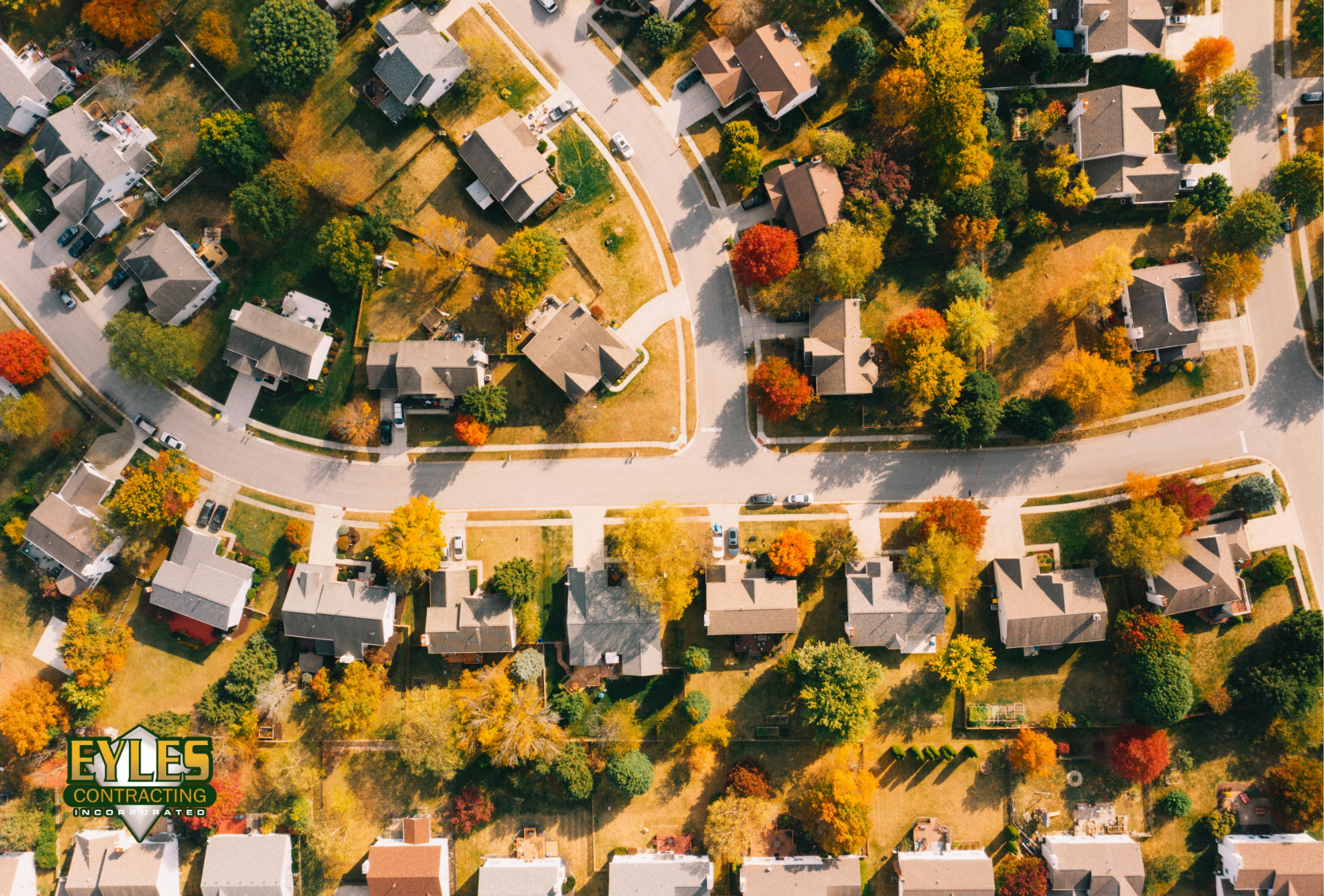 An aerial view of a residential neighborhood in fall with colorful autumn trees and rooftops visible