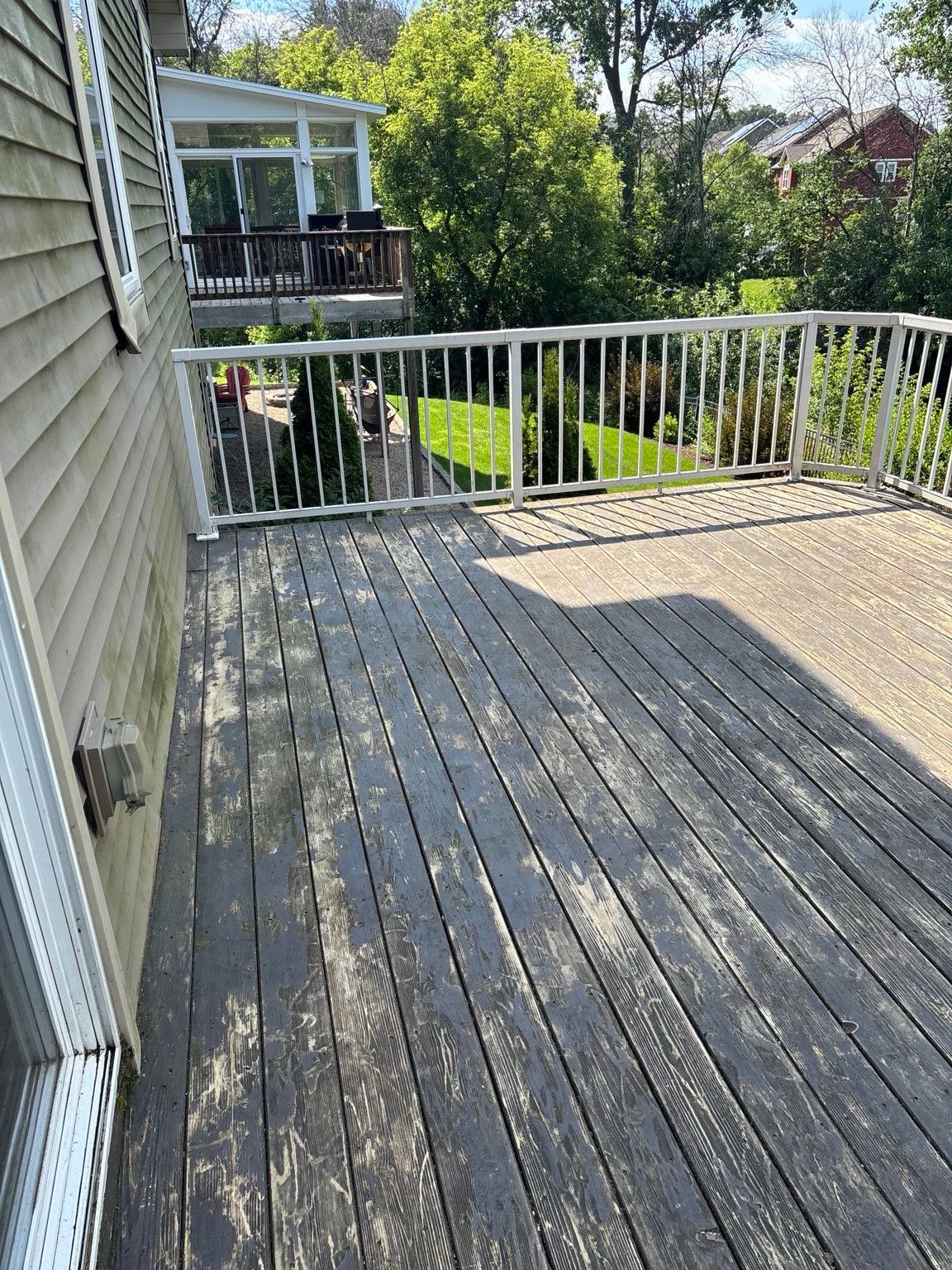 Weathered deck boards beside house siding and white railings.