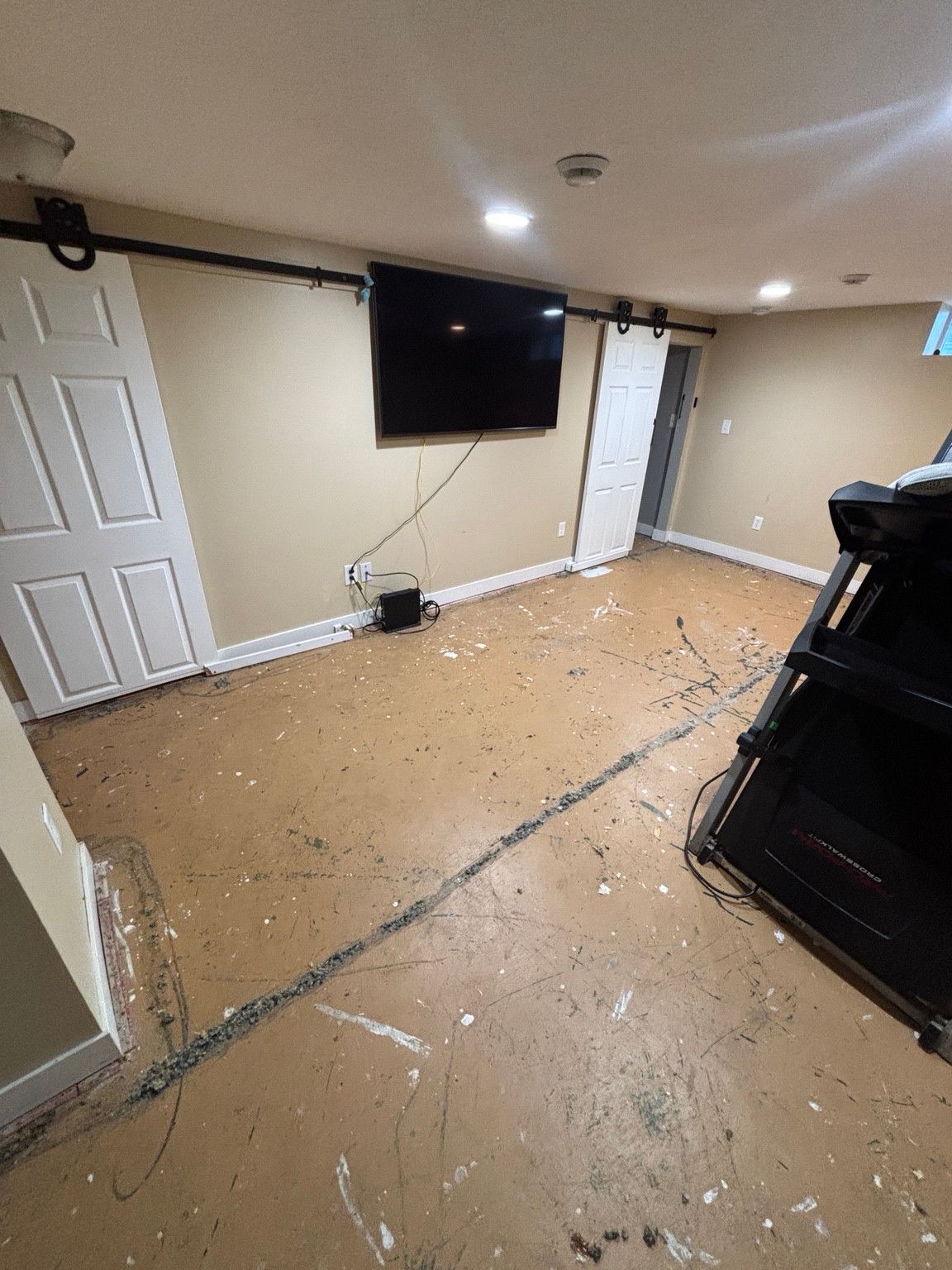 Basement room with exposed flooring, white sliding doors and a wall-mounted television.