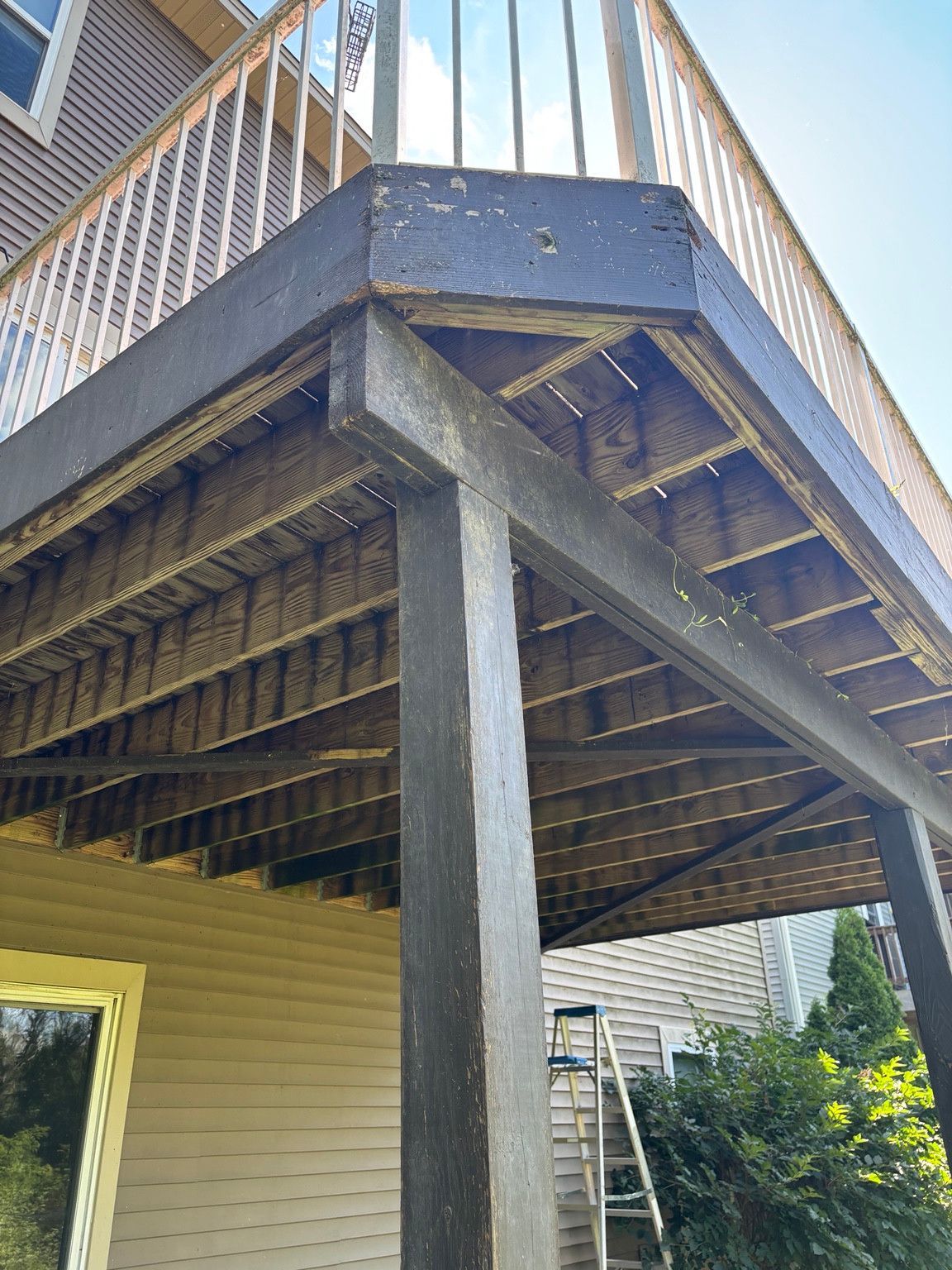 Underside of an elevated wood deck with weathered fascia, beams and support posts.