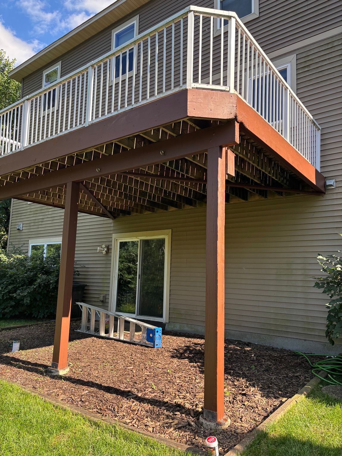 Elevated wood deck with reddish-brown fascia and support posts beneath white railings.
