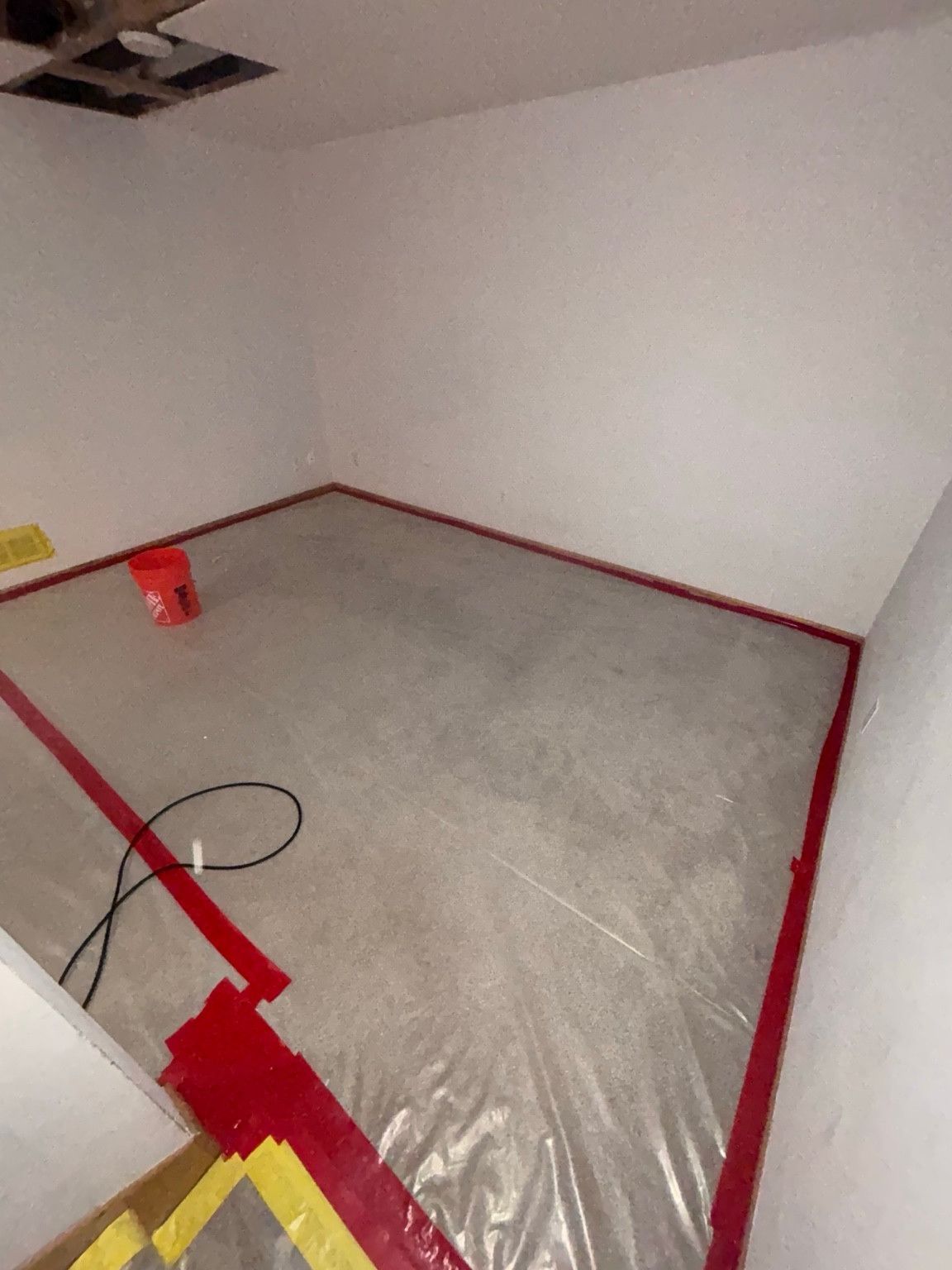 Room with protective plastic secured across the floor beneath a ceiling opening.