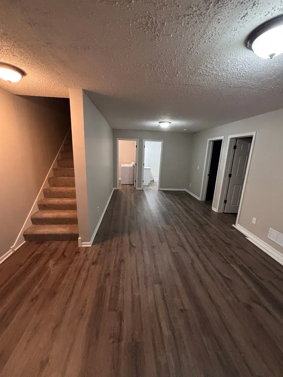 Lower-level interior with wood-look flooring, gray walls, white trim, and carpeted stairs