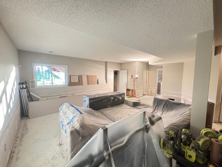 Basement drywall repair in progress with lower-wall joints treated and furniture protected.