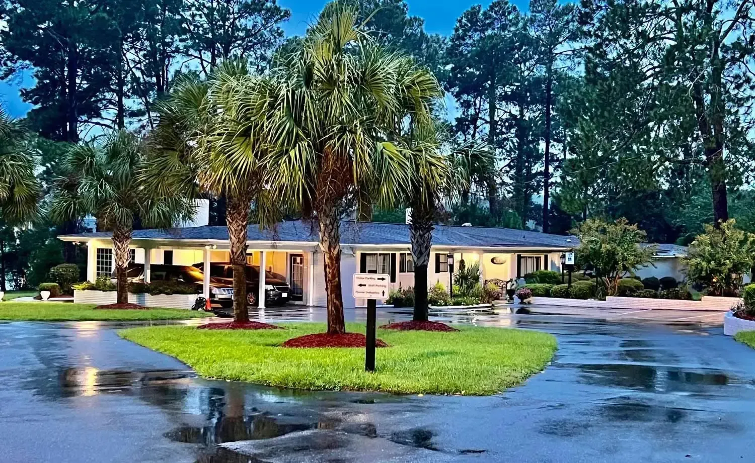 Single-story house with palm trees and wet driveway at dusk
