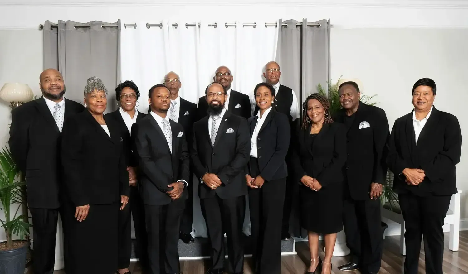 Group of people in black suits posing indoors in front of gray curtains