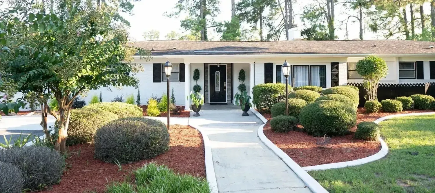 Single-story house with white columns, curved walkway, and landscaped front yard