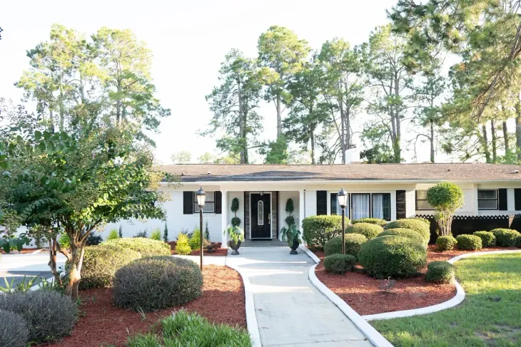 Single-story suburban house with white trim, front walkway, and landscaped yard