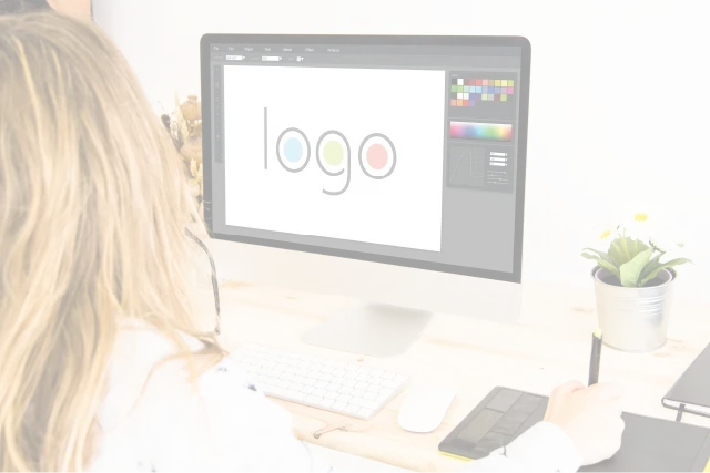 A woman is sitting at a desk looking at a computer screen with the word logo on it.