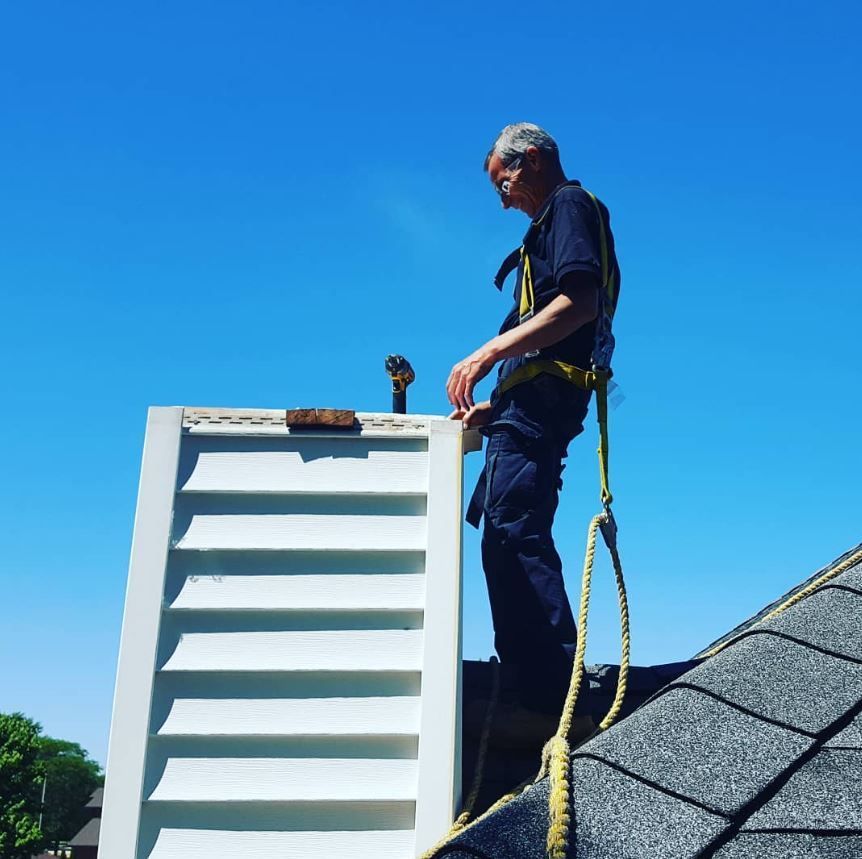 A man standing on top of a roof holding a white shutter