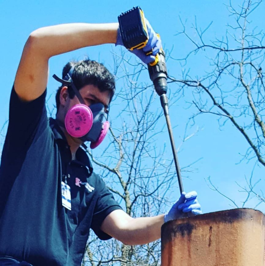 A man wearing a mask and gloves is using a drill