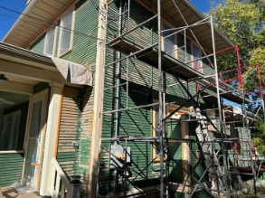 Green house under renovation with scaffolding. Peeling paint and covered windows visible.