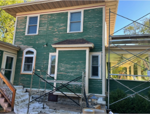 Green house exterior with peeling paint; scaffolding alongside.