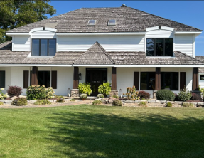 White house with brown roof, shutters, and columns. Green lawn and landscaping in front.