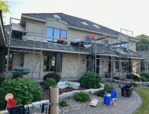 Workers on scaffolding renovating a two-story beige house with a dark roof.