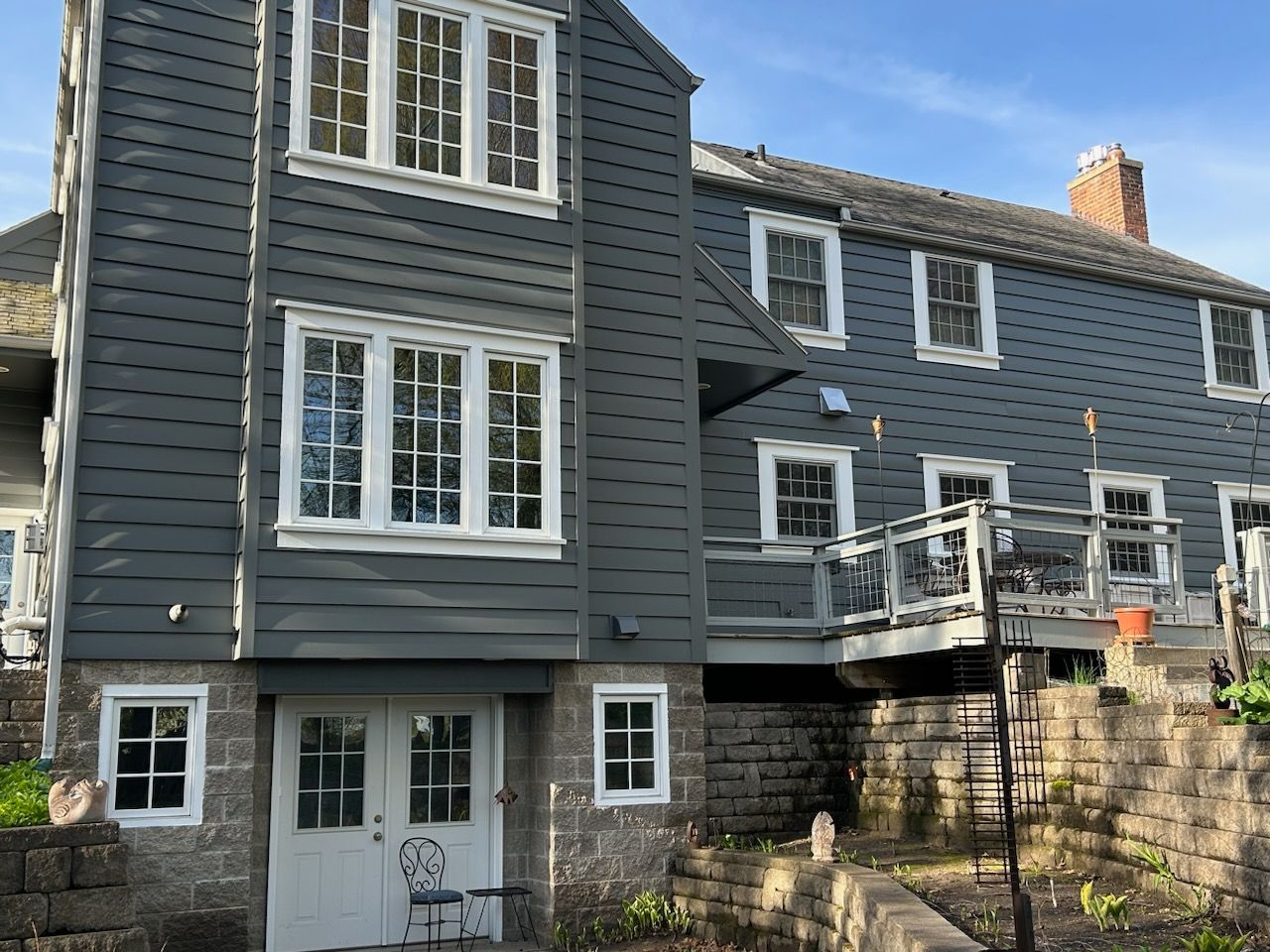Gray building with white-trimmed windows and doors, possibly a mill, adjacent to a stone structure with a wooden deck.