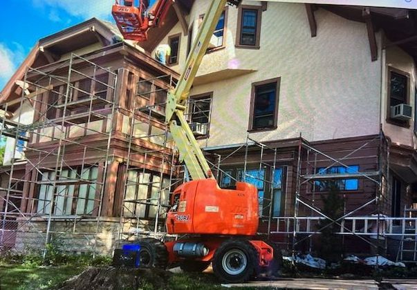 A two-story house under renovation with scaffolding, an orange lift, and workers.