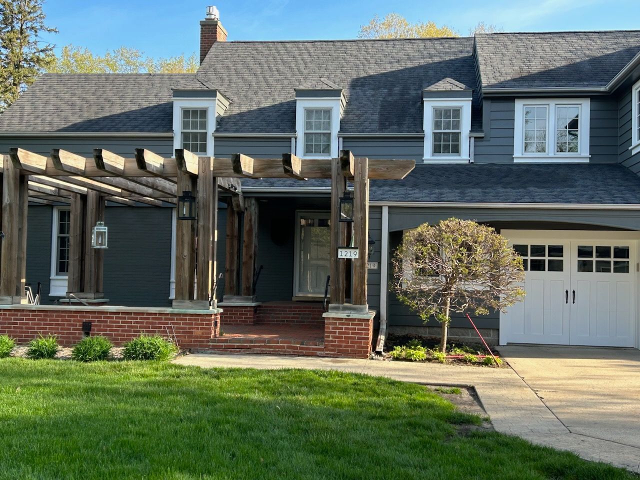 Blue house with white trim, pergola, and white garage door. Green lawn in front.