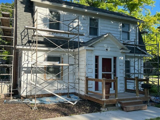 Two-story white house with scaffolding, undergoing renovations. Features a red door and porch.
