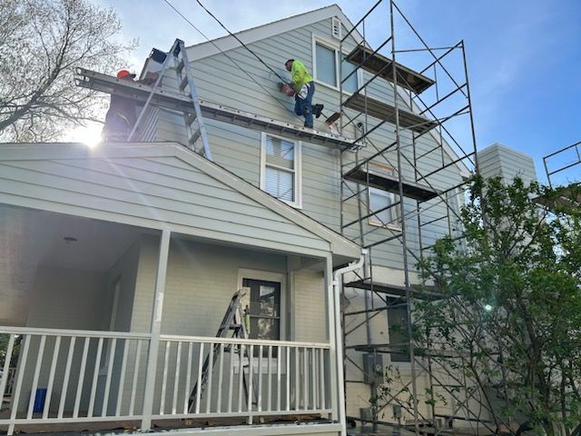 Construction worker on scaffolding, repairing siding on a two-story house, sunny day.