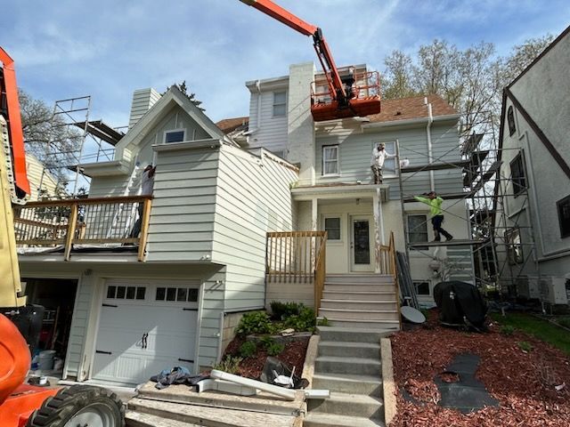 Workers on scaffolding and lift repairing a two-story house with a garage and porch.