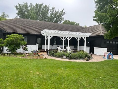 Black house with white pergola, patio, and green lawn.