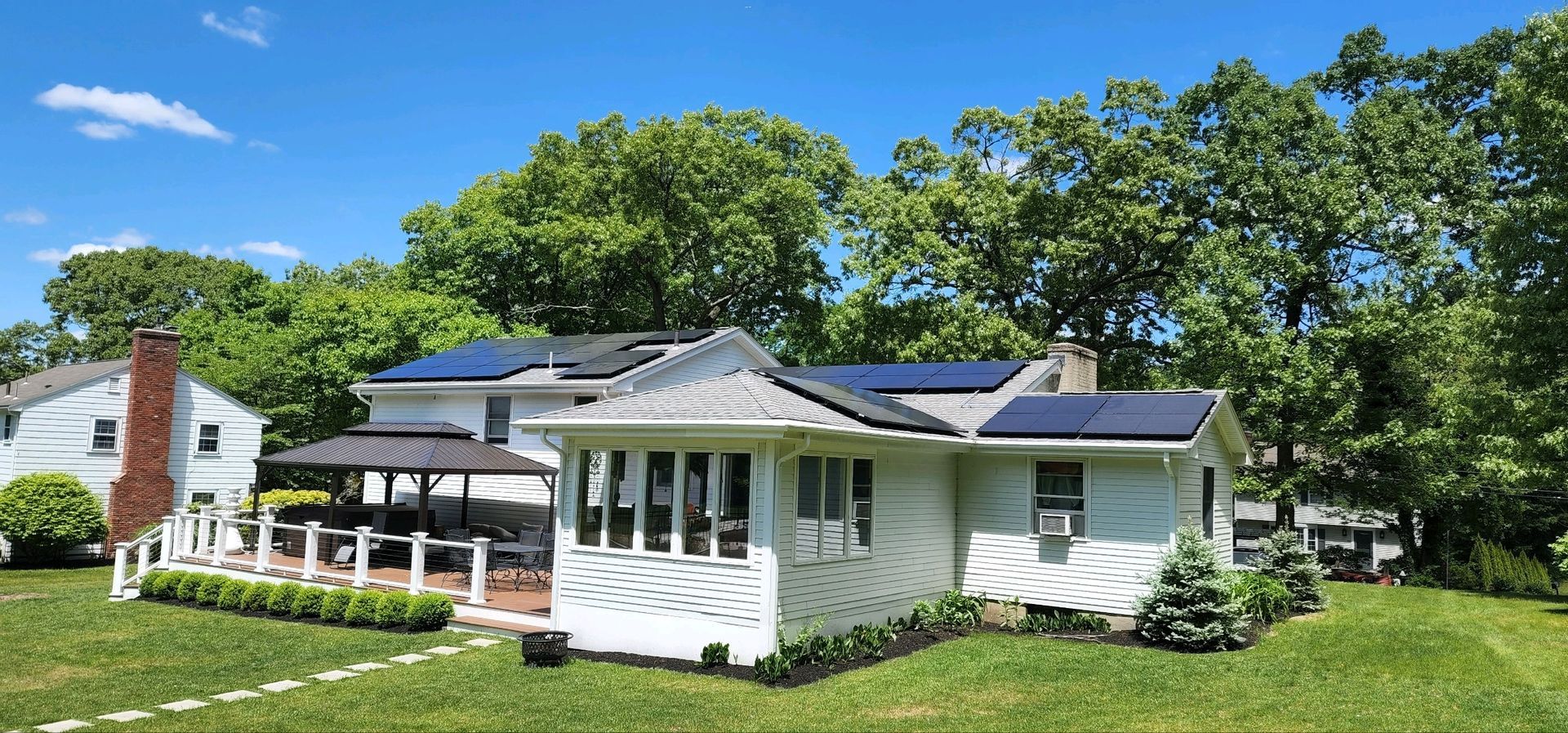 White house with green roof and front porch on a sunny lawn, framed by trees and blue sky