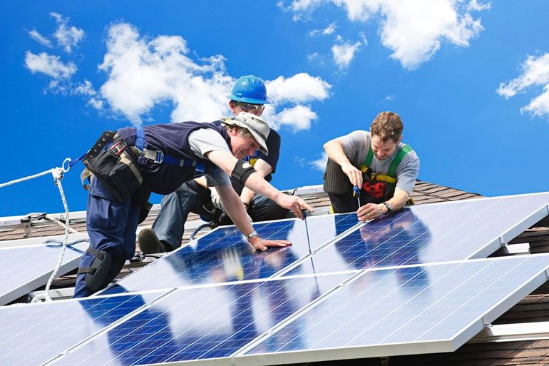 Workers installing solar panels on a rooftop under a bright blue sky