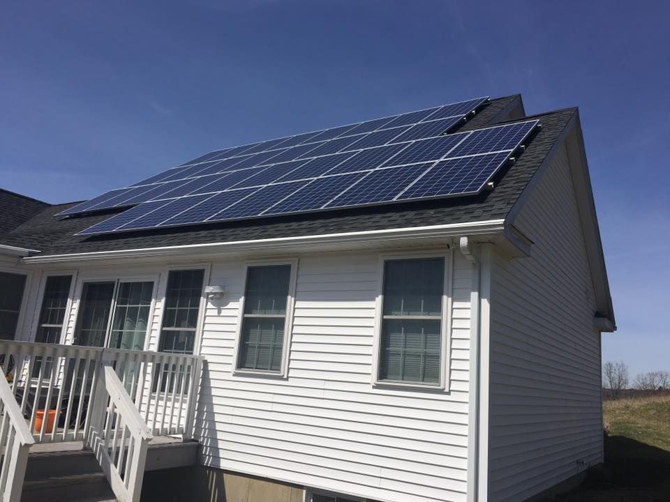 White house with solar panels on the roof under a clear blue sky.