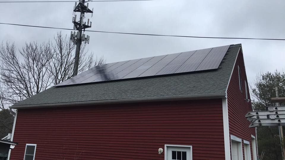 Red barn with solar panels on the roof beside utility poles under an overcast sky