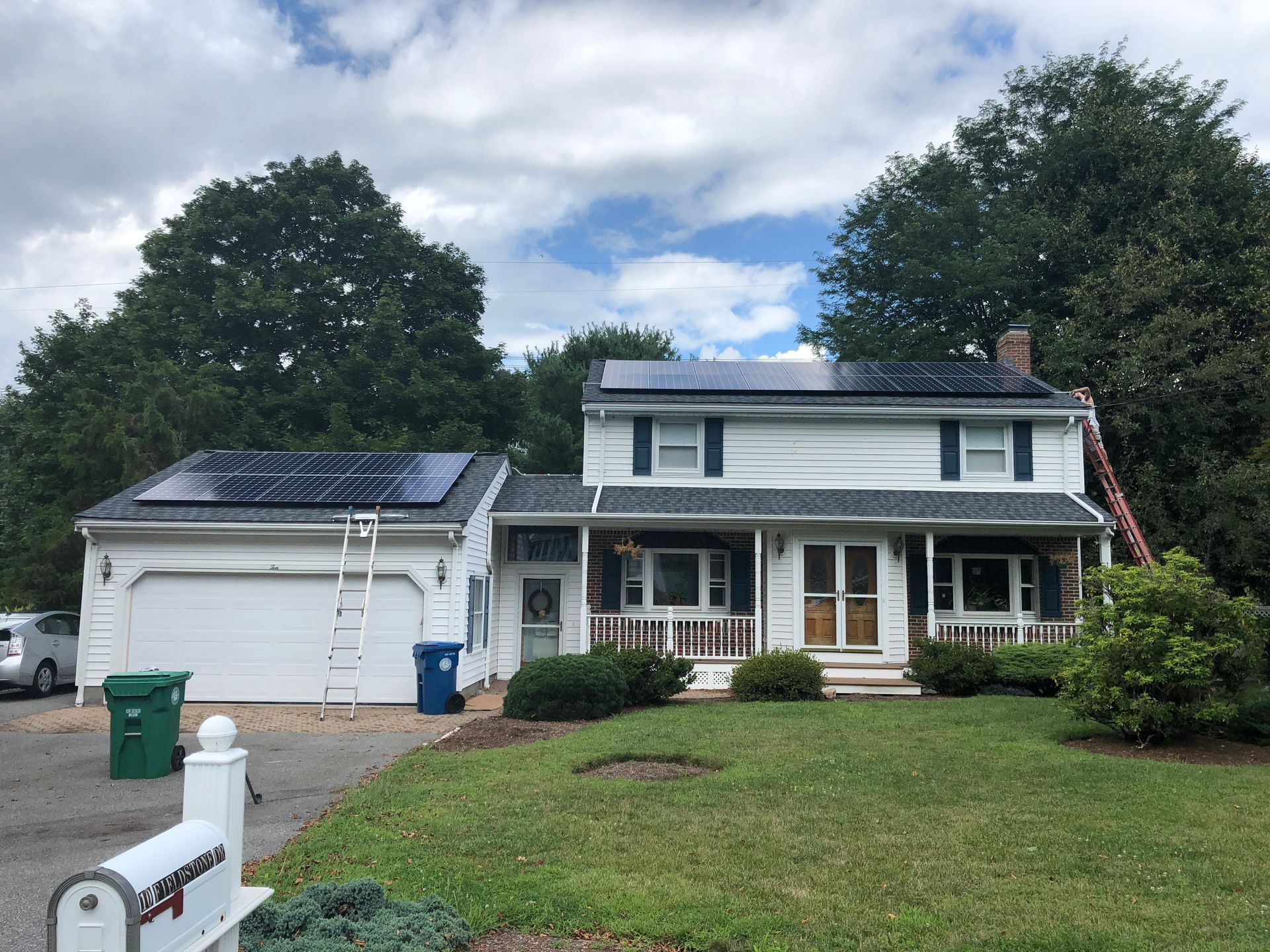 Suburban house with white siding, two-car garage, front porch, and solar panels on the roof.