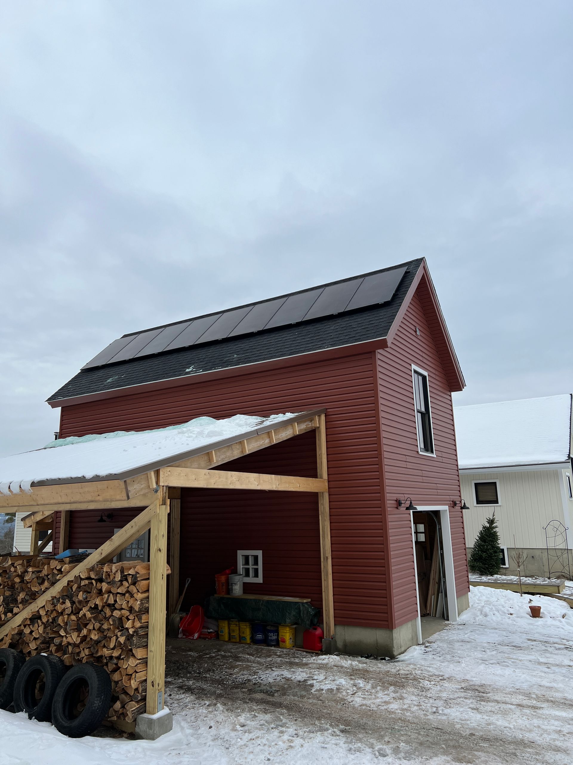 Red house with solar panels and woodpile under a snowy sky