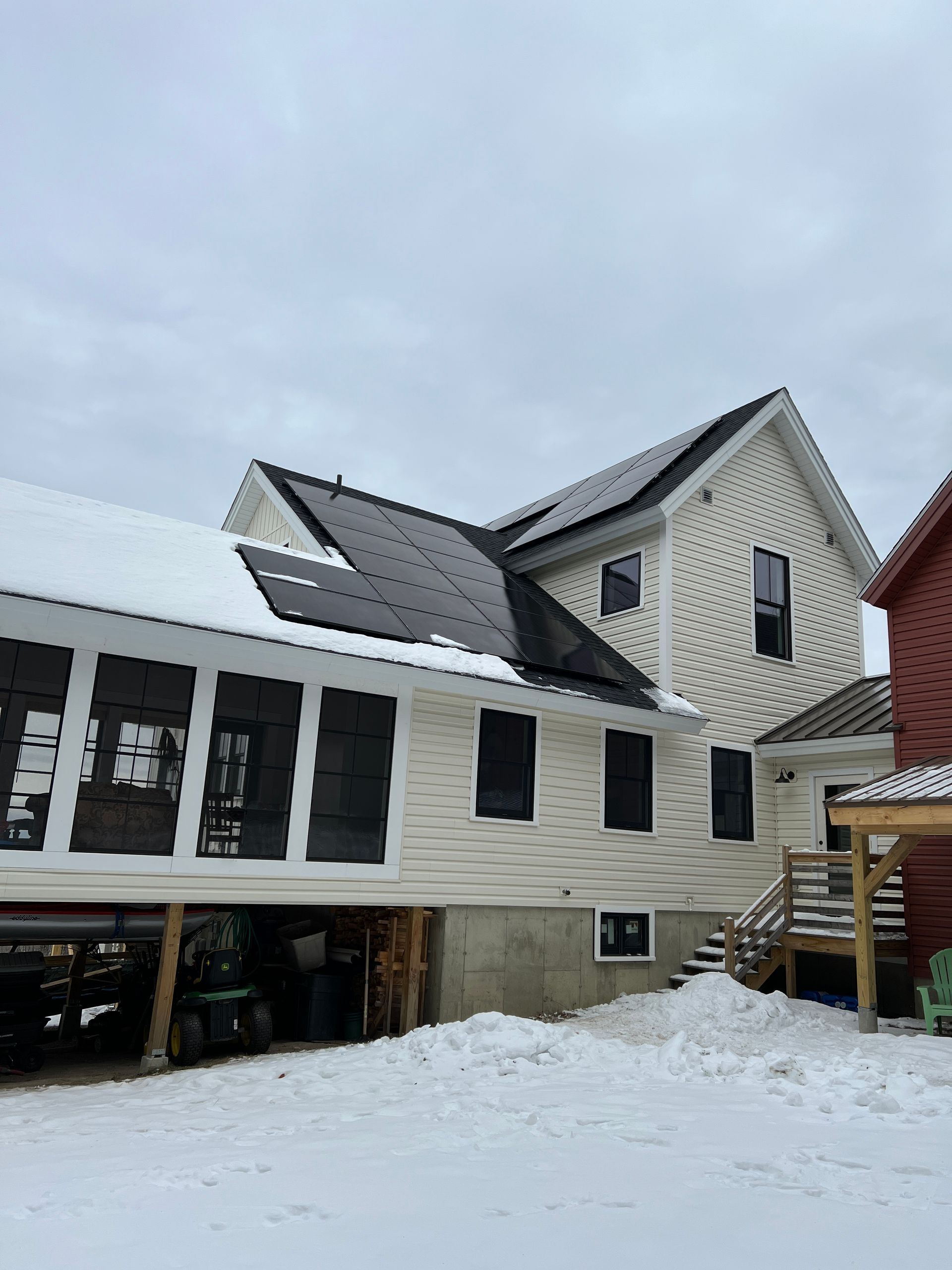 Snow-covered house with solar panels and a garage under construction