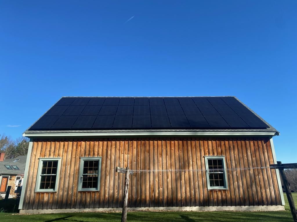 Weathered wooden barn with a black solar-panel roof under a clear blue sky